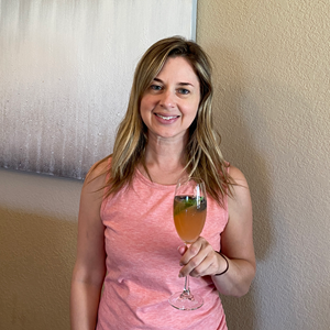 woman in front of gray painting holding cocktail in tall wineglass with berry and mint garnishes