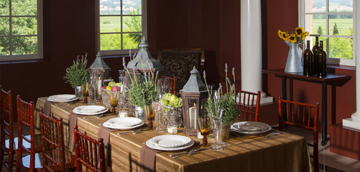 A table setting decorated with lanterns and lavender in a private Geyserville tasting room. A bar cart is nearby with a vase of sunflowers and 3 wine bottles.