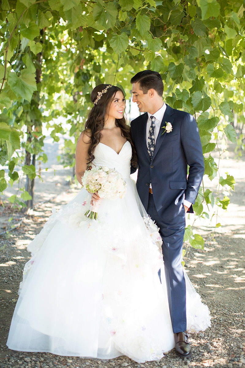 A closeup of a bride and groom posing beneath an arbor of grape leaves at a wedding venue in Sonoma wine country.