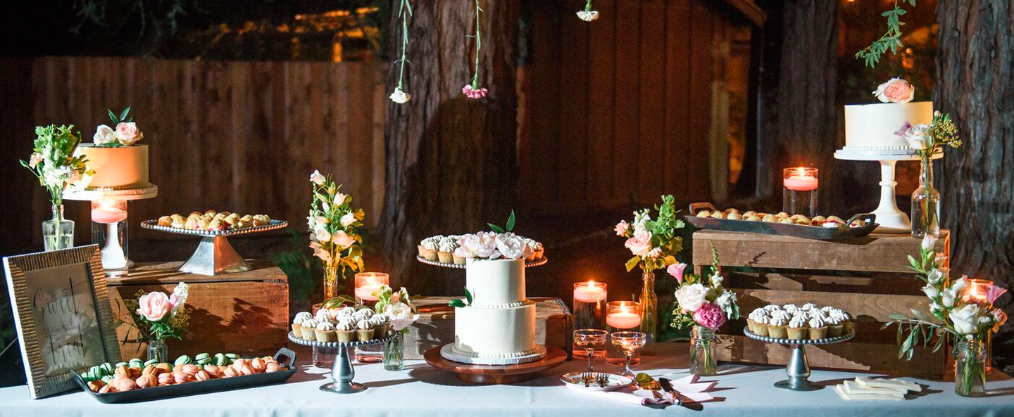 An aerial view of a banquet table with wedding desserts like cupcakes, macaroons and cake framed by hanging flowers and trees at Trentadue’s wedding venue.