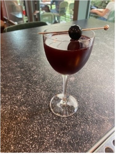 dark cocktail in a glass with a skewered cherry on top
