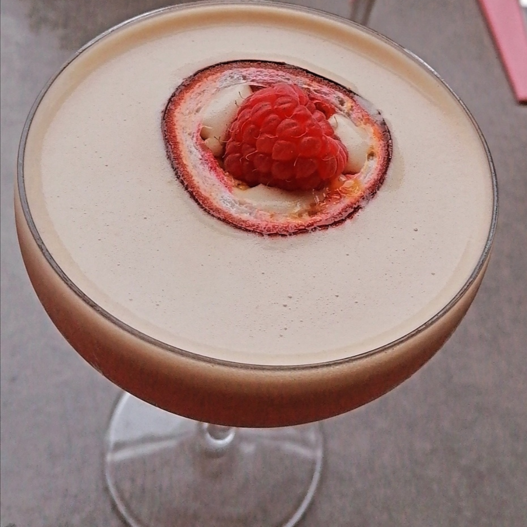 cocktail in coupe glass from the top with foam top garnished with raspberry