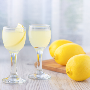 light yellow cocktail in small brandy glass with lemon garnish and three lemons on the side