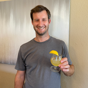 man holding a cocktail in his hand with a lemon garnish