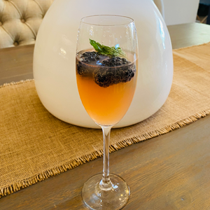 peach colored cocktail in skinny wine glass with berries and mint garnish on a table